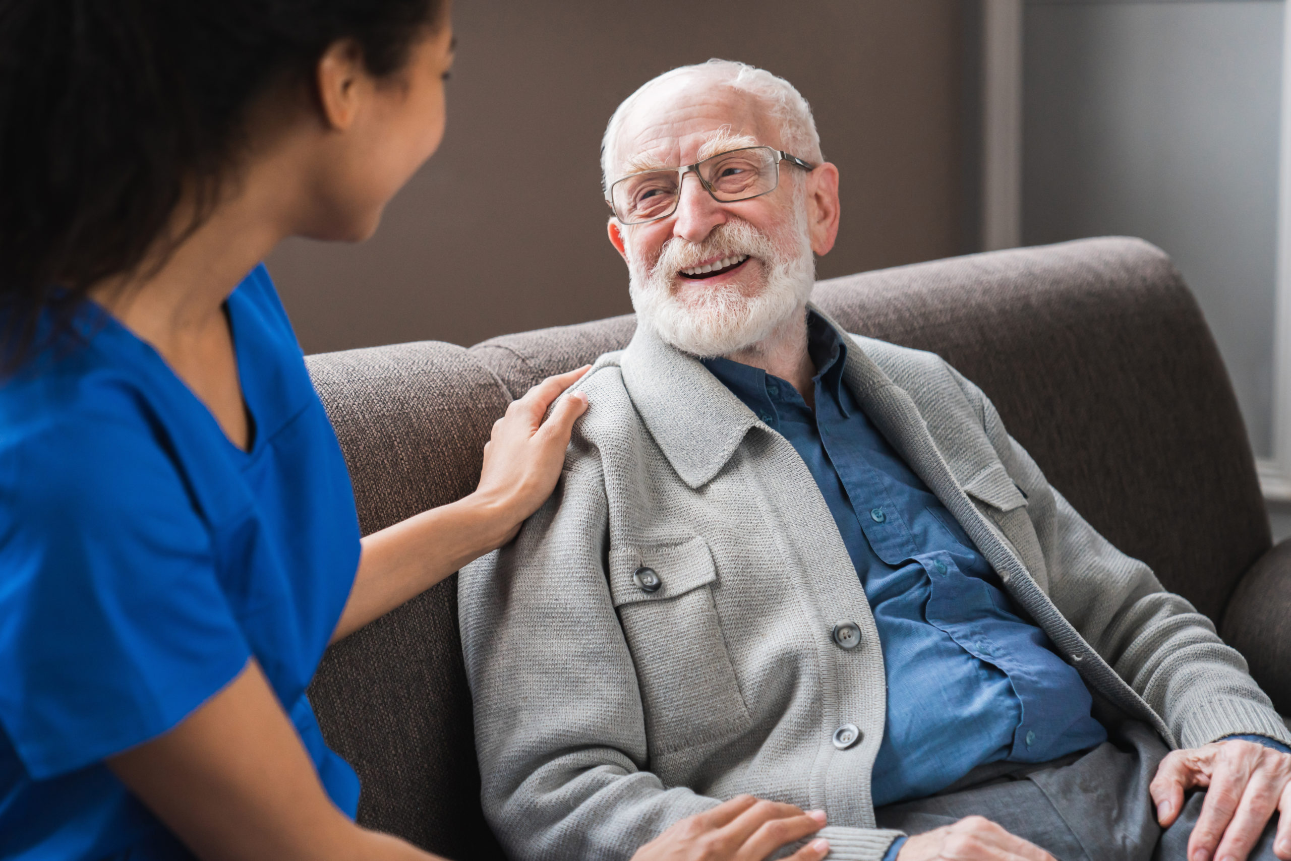 Friendly female caregiver talking chatting to happy senior man in hallway of nursing home.